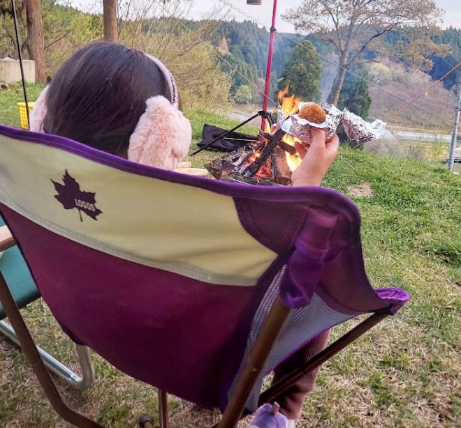 ロゴスのバケットチェアに座って焼きおにぎりを食べる娘