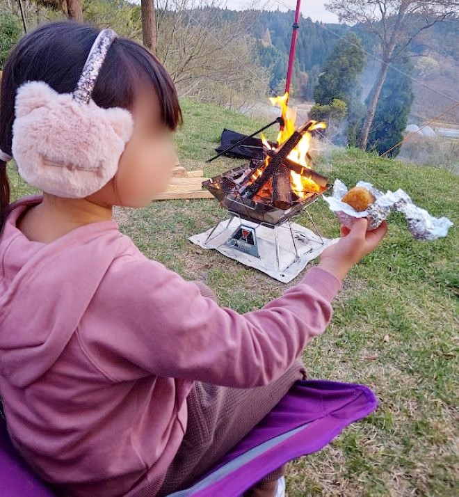 焚き火をしながら焼きおにぎりを食べる女の子